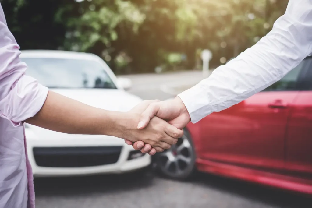 Zwei Menschen geben sich die Hand vor zwei Autos nach einem Unfall im Freien