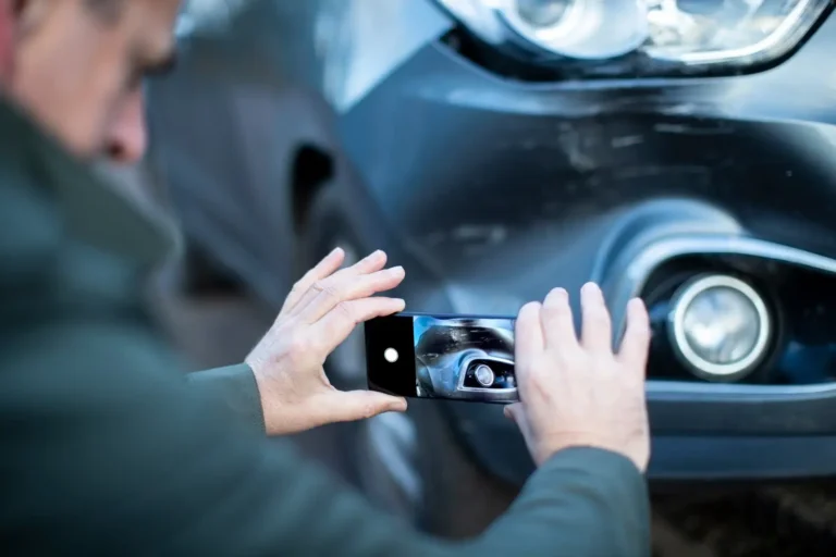 Ein Mann fotografiert mit konzentriertem Blick einen Kratzer an einem silbernen Auto